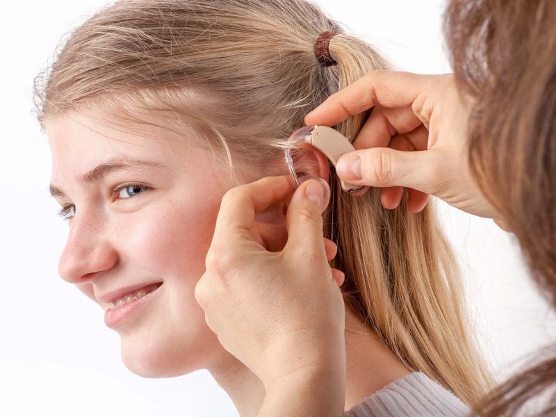 Woman inserting a hearing aid into a young girl's ear in front of a white background