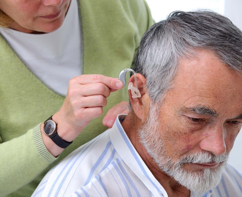 Doctor inserting hearing aid in senior's ear